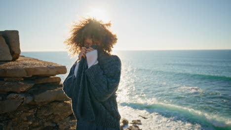 sunlight portrait curly woman smiling at ocean rocky coast. happy lady posing