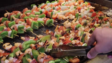 person grilling shrimp skewers on a grill with tongs hot food