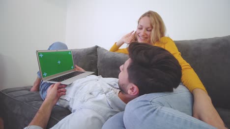 una pareja enamorada en un sofá mirando una computadora portátil. un niño tendido en el regazo de una niña. pantalla verde.