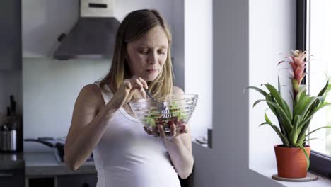 cheerful pregnant woman eating healthy food at kitchen