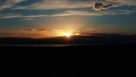 stunning aerial drone shot of a gorgeous orange sunset dipping under a mountain by utah lake in utah valley, usa