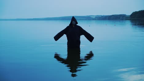 terrible figure in a black robe in the water outdoor. divination by halloween