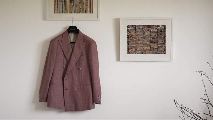 Blazer doppiopetto rosa appeso a una parete con opere d'arte incorniciate.