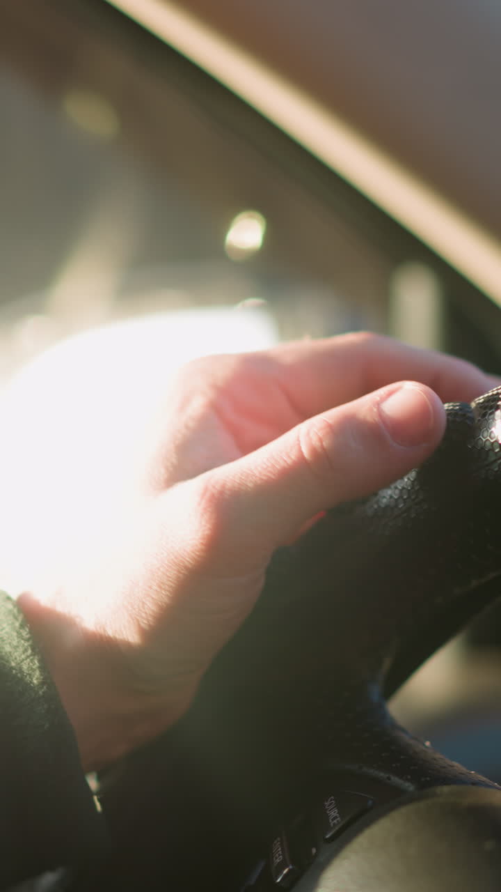 차의 스티어링 을 잡고 는 사람의 손의 클로즈업, 빛이 창문을 통해 필터링되어 운전자의 집중과 기대를 강조합니다.