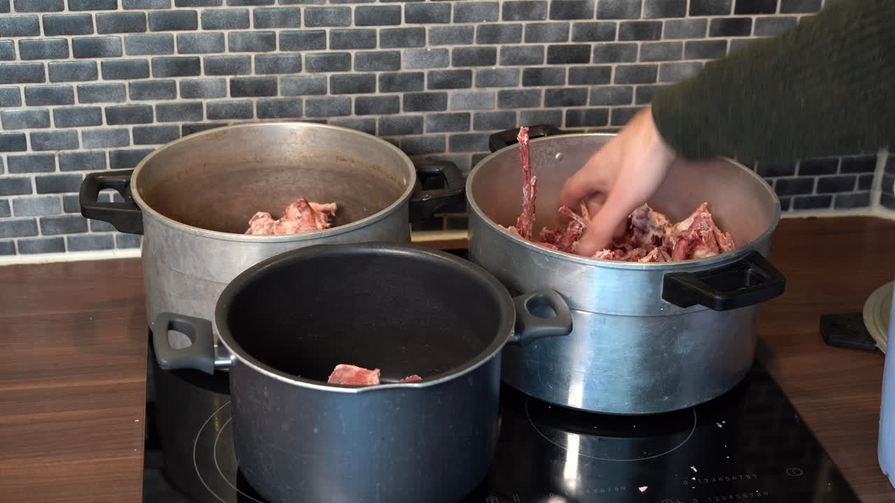 Hand arranging raw beef bones in various pots for boiling bone broth