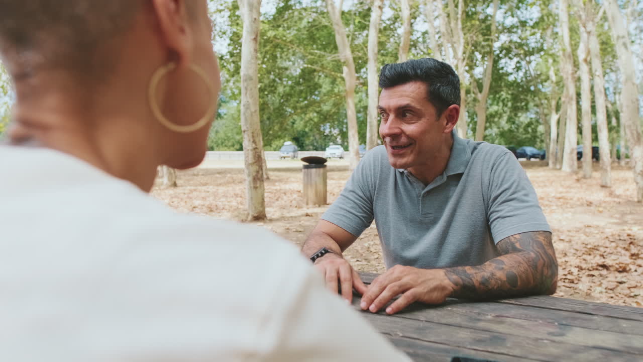 Uomo e donna che conversano amichevolmente a un tavolo da picnic nel parco
