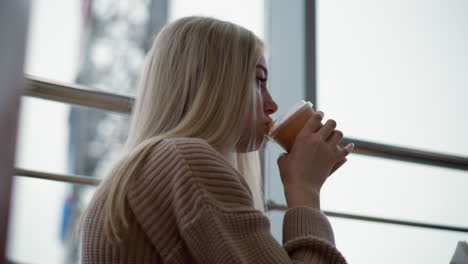 close-up of woman sipping beverage in shopping mall with blurred background featuring iron rail, creating cozy atmosphere with casual lifestyle moment in a modern setting