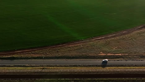 Aerial-shot-of-car-driving-on-dirt-road-in-near-pivots-with-green-farm-growth-in-Willcox,-Arizona,-wide-side-angle-drone-shot