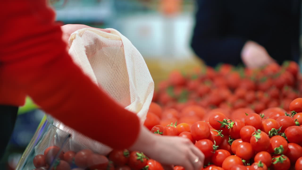 Woman picking cherry tomatoes in a reusable bag in a store. Ecology and Earth Day thematics