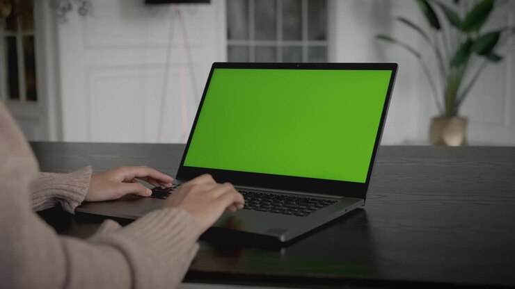 Woman with laptop on the table, green mockup screen