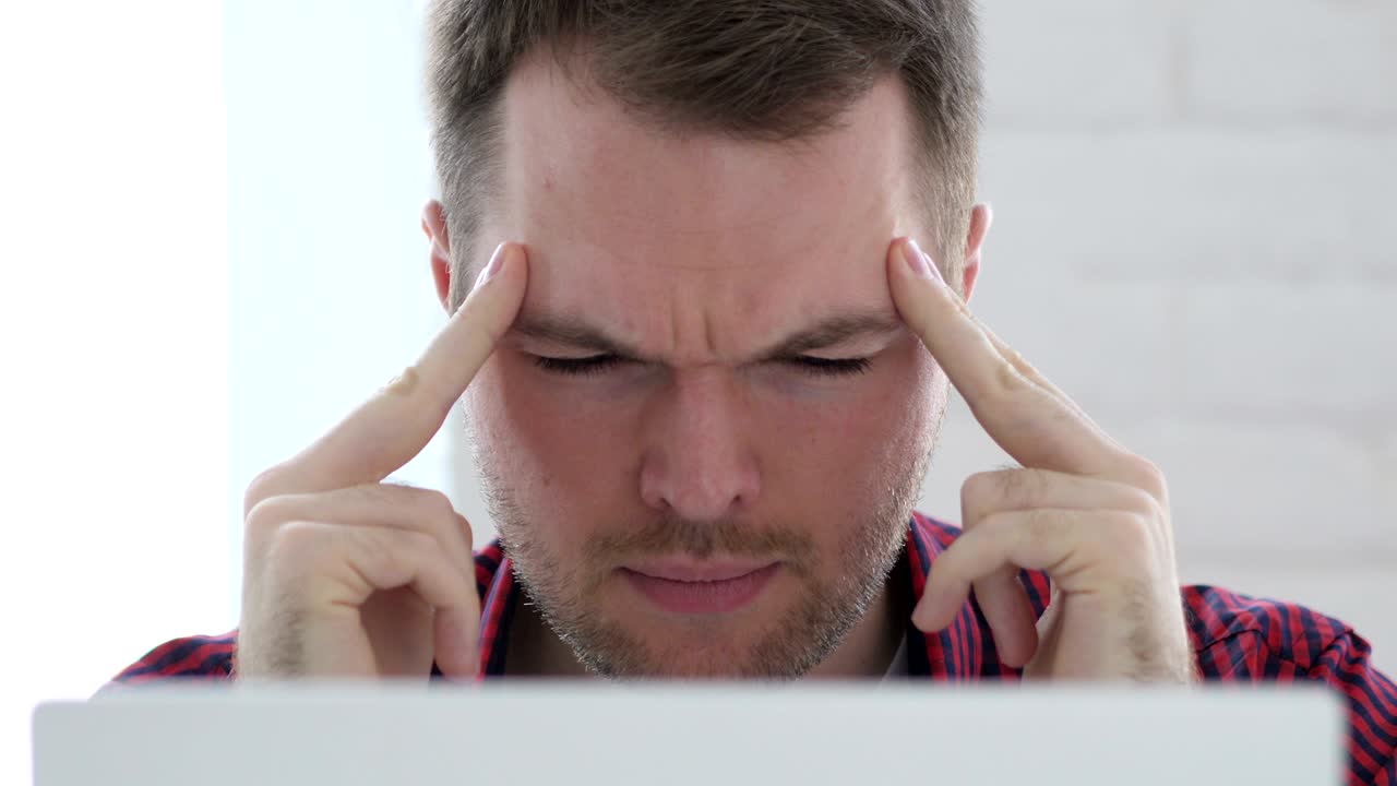 dolor de cabeza, joven molesto trabajando en la oficina de cerca