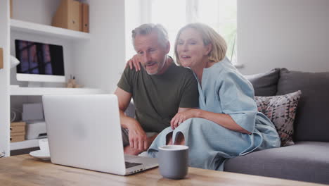 Pareja-Mayor-Sentada-En-Un-Sofá-En-Casa-Haciendo-Videollamadas-Usando-Una-Computadora-Portátil-Juntos