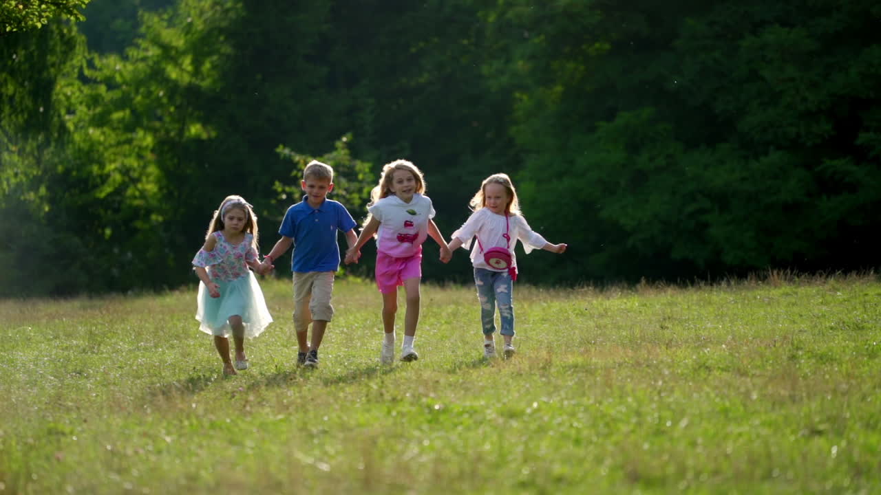 Kinder rennen draußen im Park auf grünem Gras. Süße Kinder halten Händchen und sind gut gelaunt im Park. Sonniger Sommertag im Freien.