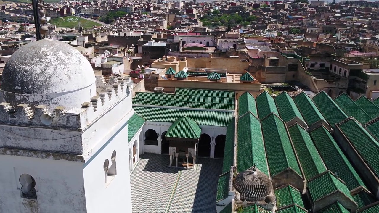 Prospettiva elevata dall'alto con drone che mostra il cortile rettangolare, la fontana in marmo, il minareto bianco e i tetti geometrici in tegole smaltate verdi della Moschea Al Quaraouiyine a Fez, Marocco