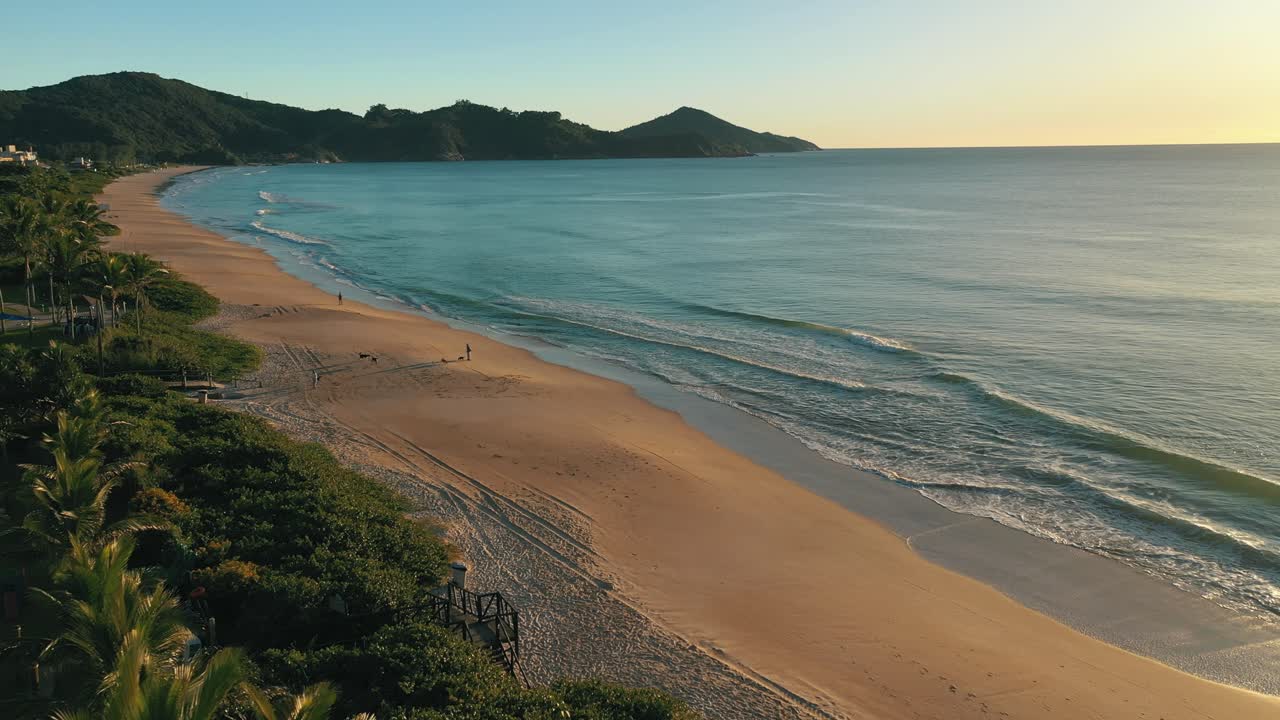 Vista aérea de drone com movimento lateral sobre praia paradisíaca ao nascer do sol, América do Sul, Bombinhas, Brasil