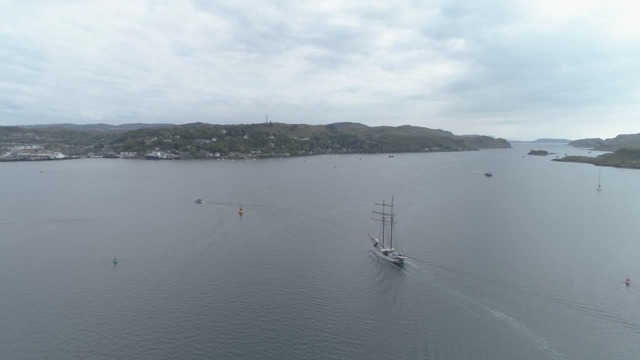 fotografía aérea de un barco alto llegando a la bahía de oban, escocia, en un día nublado