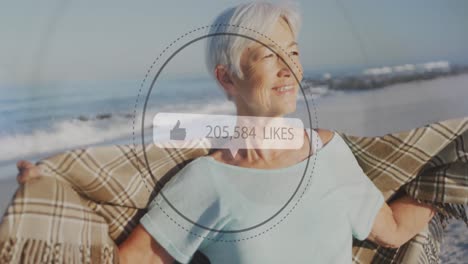 Animation-of-speech-bubble-with-thumbs-up-icon-and-numbers-over-senior-woman-on-beach