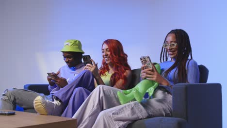 Studio-Shot-Of-Group-Of-Young-Gen-Z-Friends-Sitting-On-Sofa-Gaming-And-Using-Social-Media-On-Mobile-Phones