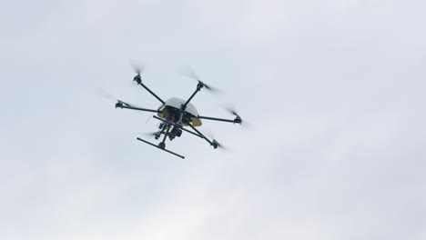 Handheld-camera-showcases-black-drone-with-spinning-rotors,-soaring-at-high-altitude-against-a-backdrop-of-a-cloudy-sky