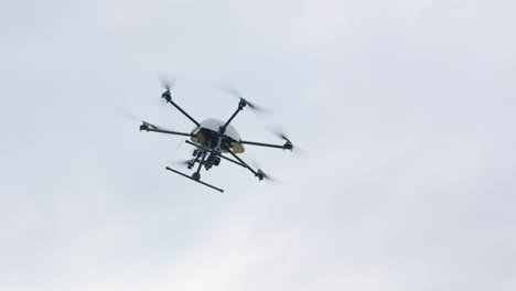 handheld camera showcases black drone with spinning rotors, soaring at high altitude against a backdrop of a cloudy sky