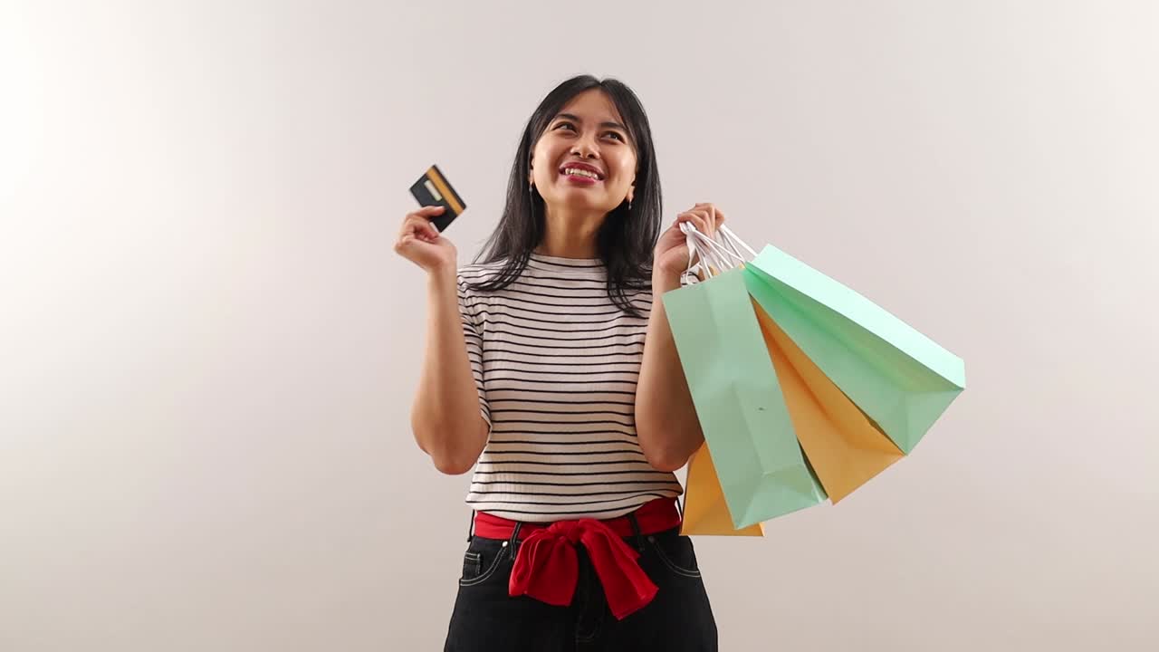 Giovane donna asiatica che mostra e presenta una carta di credito o di debito e tiene una borsa della spesa, donna d'affari che fa acquisti online, concetto finanziario.