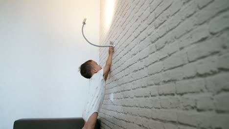caucasian toddler in white bodysuit turns on the lamp on the wall. baby plays with light at home.