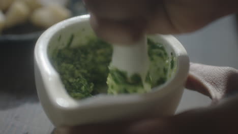 grinding herbs to make pesto in a mortar and pestle