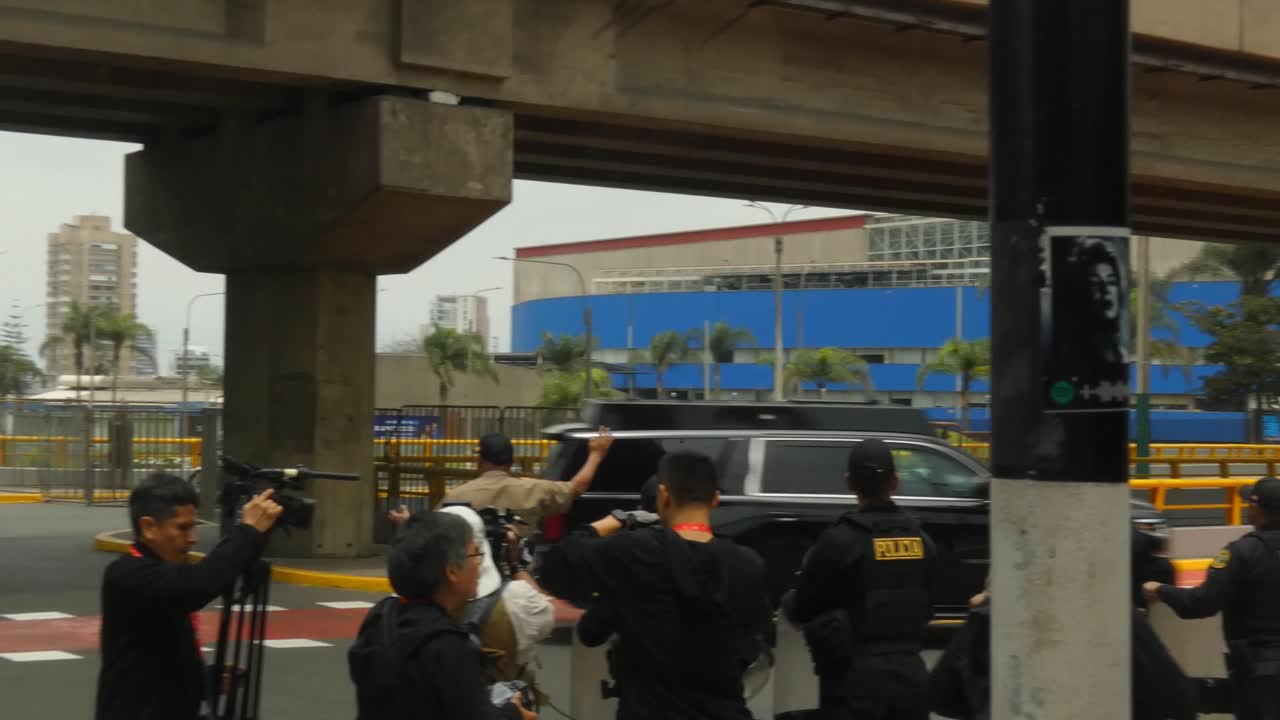 The presidential motorcade of United States president Joe Biden driving by on route to APEC 2024 summit in Lima, Peru. Many cars with red and blue lights pass by a group of people, press and policemen