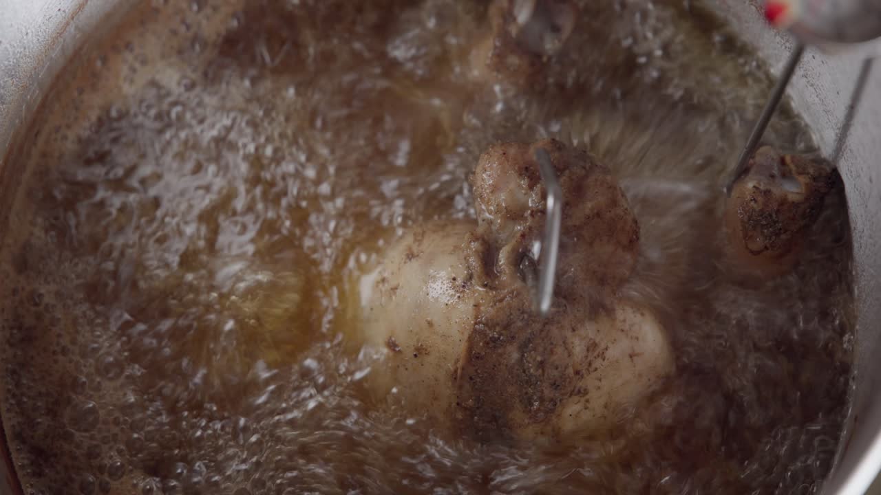 Et detaljert nærbilde av en kalkun som friteres i varm, boblende olje inni en frityrkoker. Kokende fett omgir raskt fjærfeet mens det tilberedes, noe som skaper intens tekstur, bevegelse og fresende action.