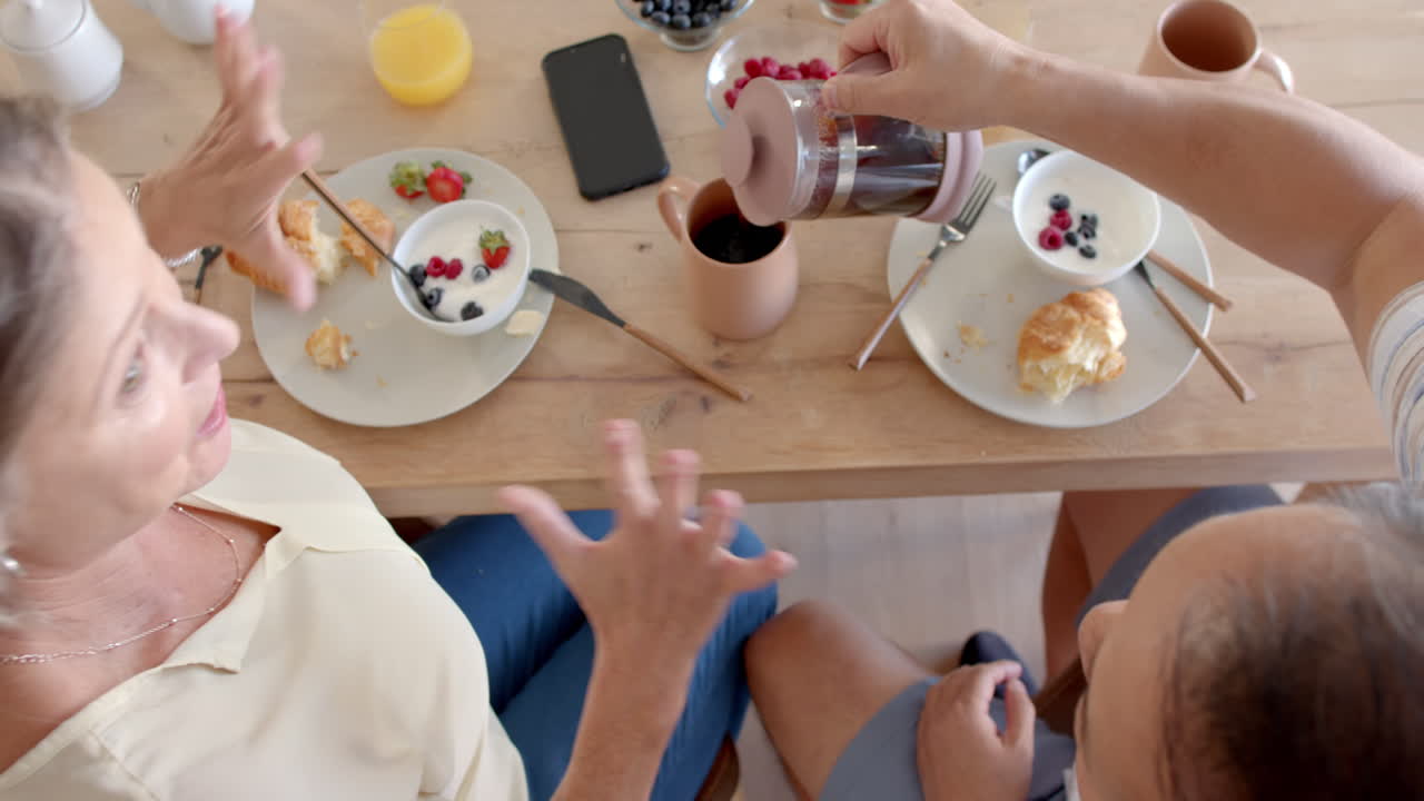Pouring coffee, senior couple enjoying breakfast with fruit and pastries on vacation