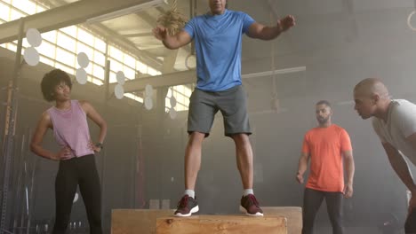 diverse group fitness class watching male coach jump onto box, cross training at gym, in slow motion