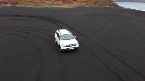 white suv driving on black sand beach on atlantic coast, iceland