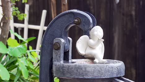 Ceramic-angel-figurine-sitting-on-top-of-a-water-pump-in-the-rain