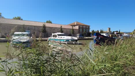 Canal-Du-Midi-At-Le-Somail-France-tourist-boat-passing-through-the-tourist-village-on-a-warm-summer-morning