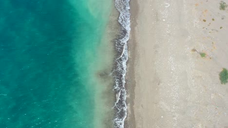 Vista-Aérea-De-Arriba-Hacia-Abajo-Con-La-Mitad-Del-Océano-Tropical-Azul-Y-La-Otra-Mitad-De-Una-Playa-De-Arena-Vacía-Con-Olas-Rompiendo-En-Un-Día-Soleado-De-Verano