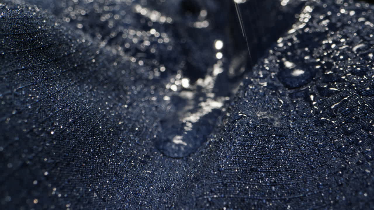 Waterproof clothing for tourism. Blue cloth texture with water drop close-up macro. Repellent waterproof breathable fabrics. Innovation waterproofing material test. High quality 4k footage