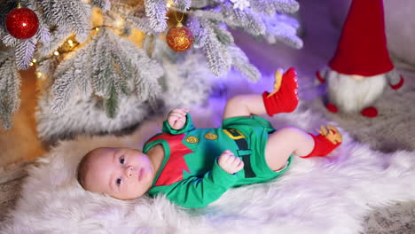 lovely sweet child wearing costume of elf and red socks with moose. adorable newborn boy lying on plaid under new year tree.