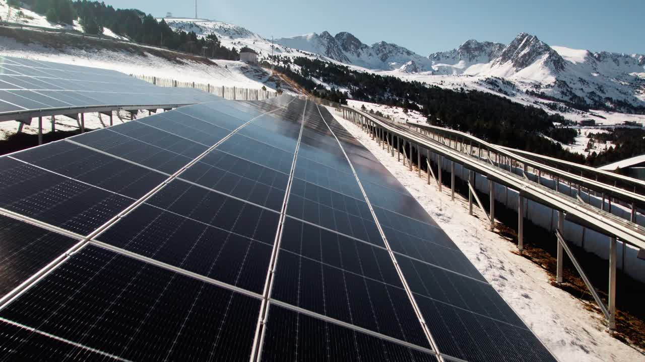 Solar panels with winter mountain landscape background, aerial close up flying over