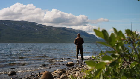 Wide-rear-shot-of-fisherman-fishing-in-lake-with-amazing-mountain-landscape