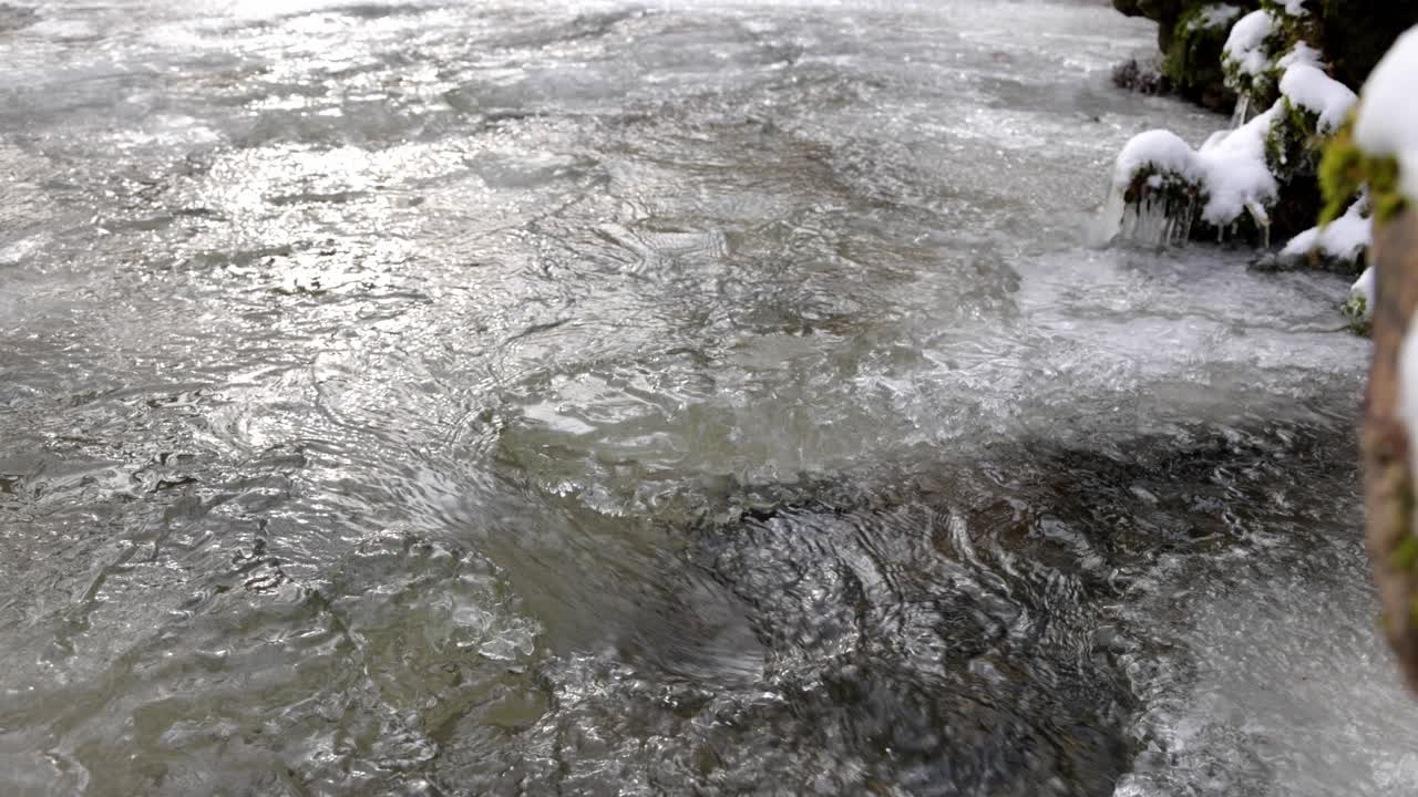 Agua fluyendo en el arroyo congelado, hielo retroiluminado