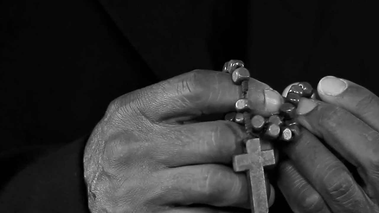 Orando a Deus com as mãos juntas, com crucifixo, com pessoas em fundo preto. Vídeo de stock.