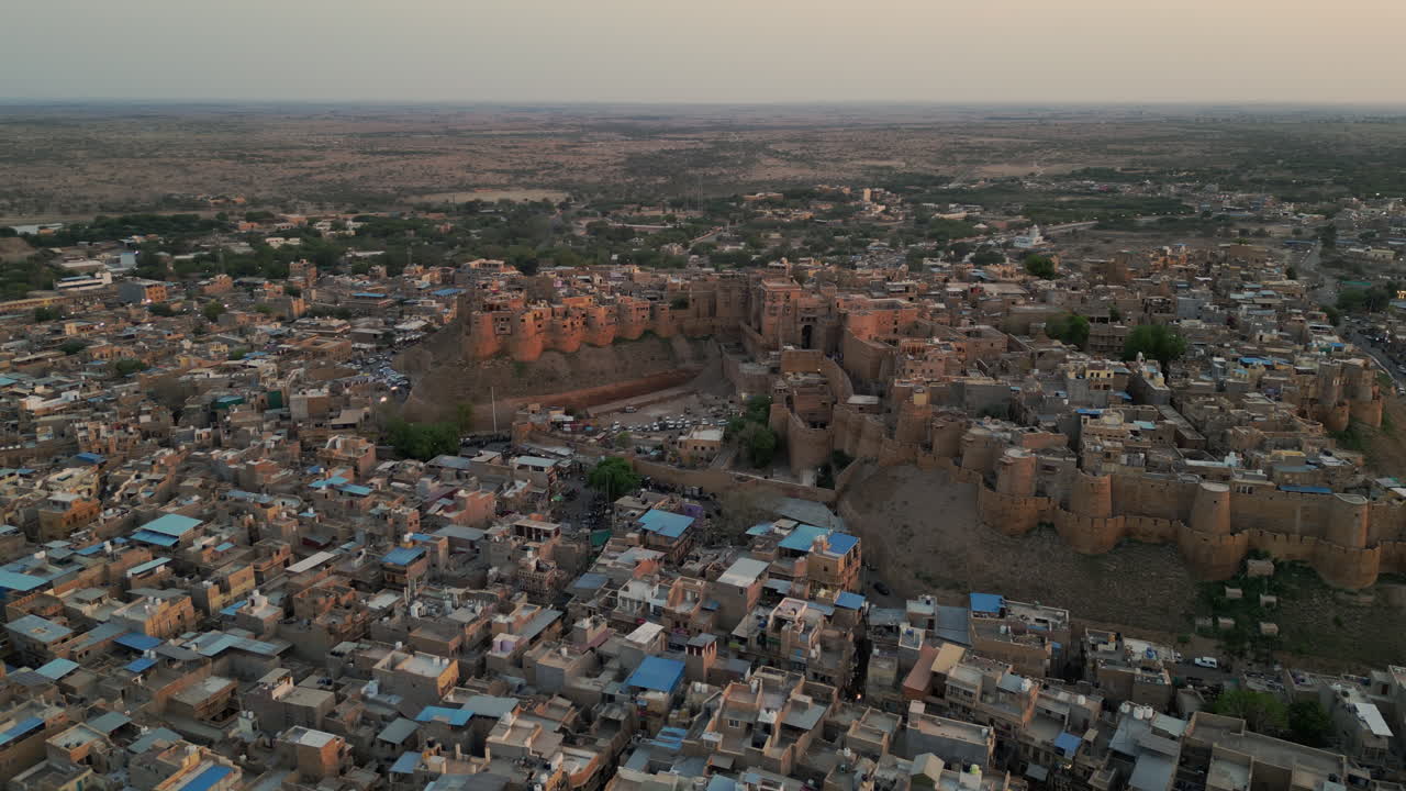 una impresionante toma de un dron en órbita de 4k del fuerte de jaisalmer al atardecer, que muestra la arquitectura de piedra arenisca dorada rodeada de casas tradicionales, con los cálidos tonos de la noche de rajasthan, india
