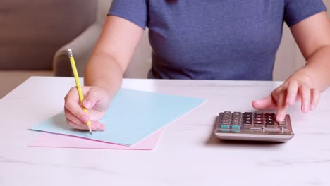 woman is using a calculator to calculate her monthly expenses and write down her monthly accounting records at home