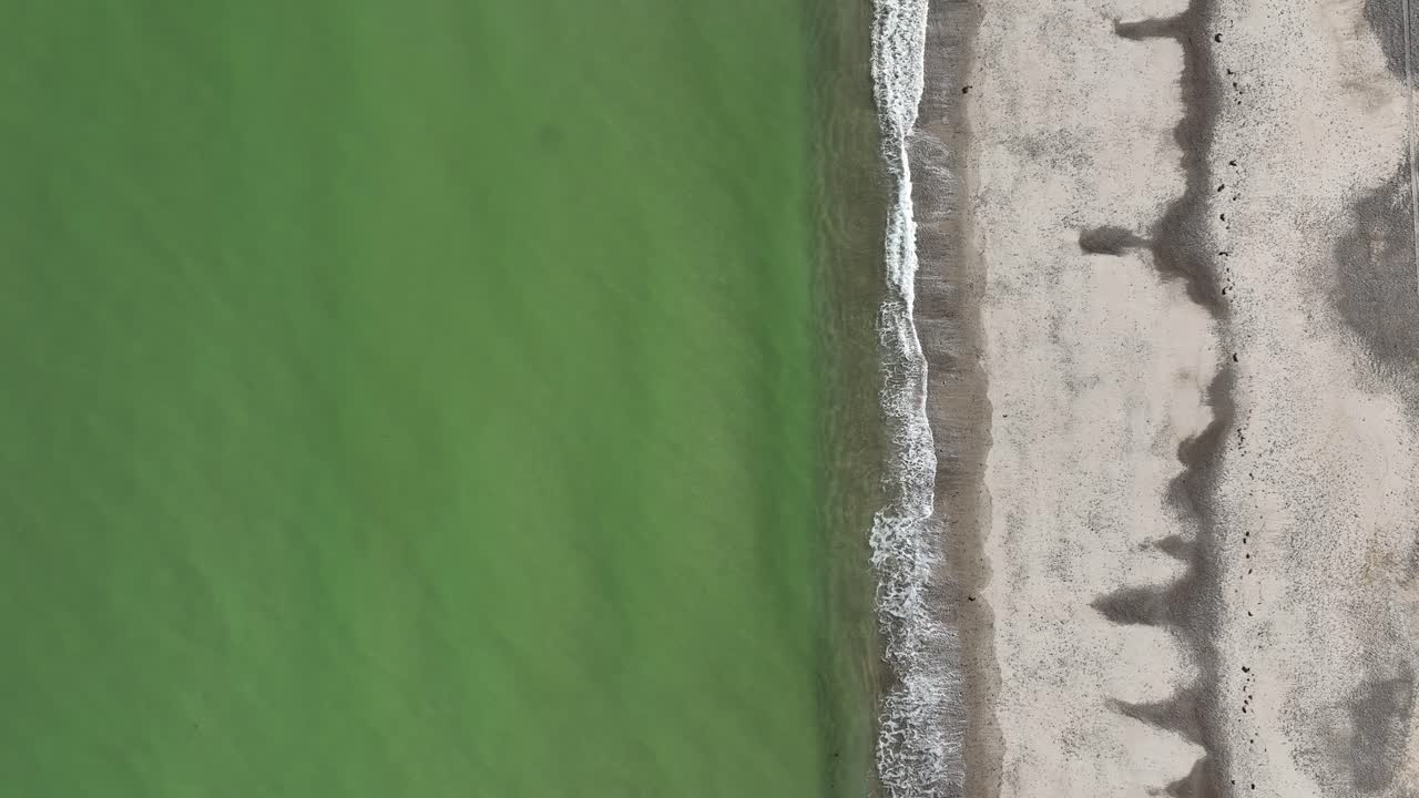 Aerial View of a Coastline with Green Water and Grey Sand
