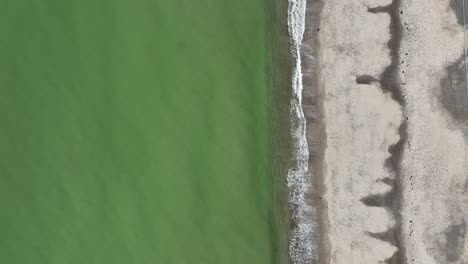 aerial view of a coastline with green water and grey sand