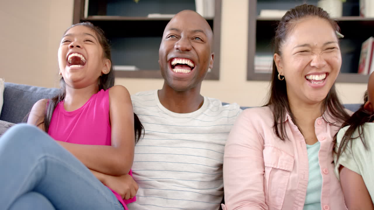 Laughing together, family of four sitting on couch enjoying time at home