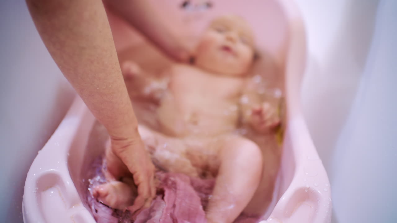 Bebé recién nacido bañándose en una bañera infantil mientras un cuidador lo sostiene y lo lava suavemente