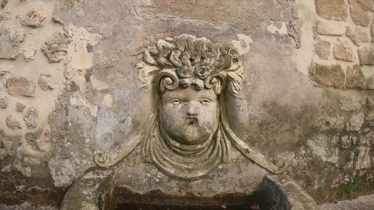 Lenta carrellata in avanti su un rilievo di mascherone in pietra erosa, scolpito in un'antica parete romana a Tivoli.