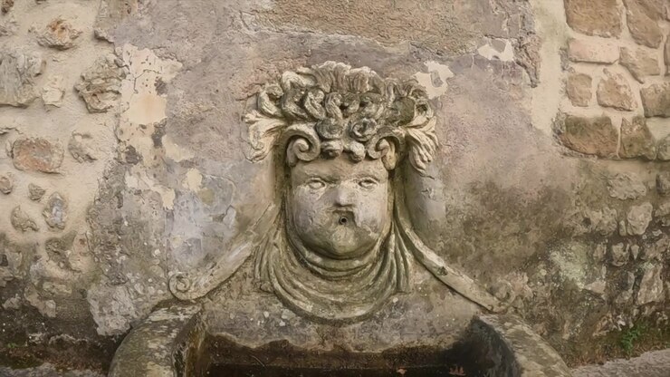 Lenta carrellata in avanti su un rilievo di mascherone in pietra erosa, scolpito in un'antica parete romana a Tivoli.