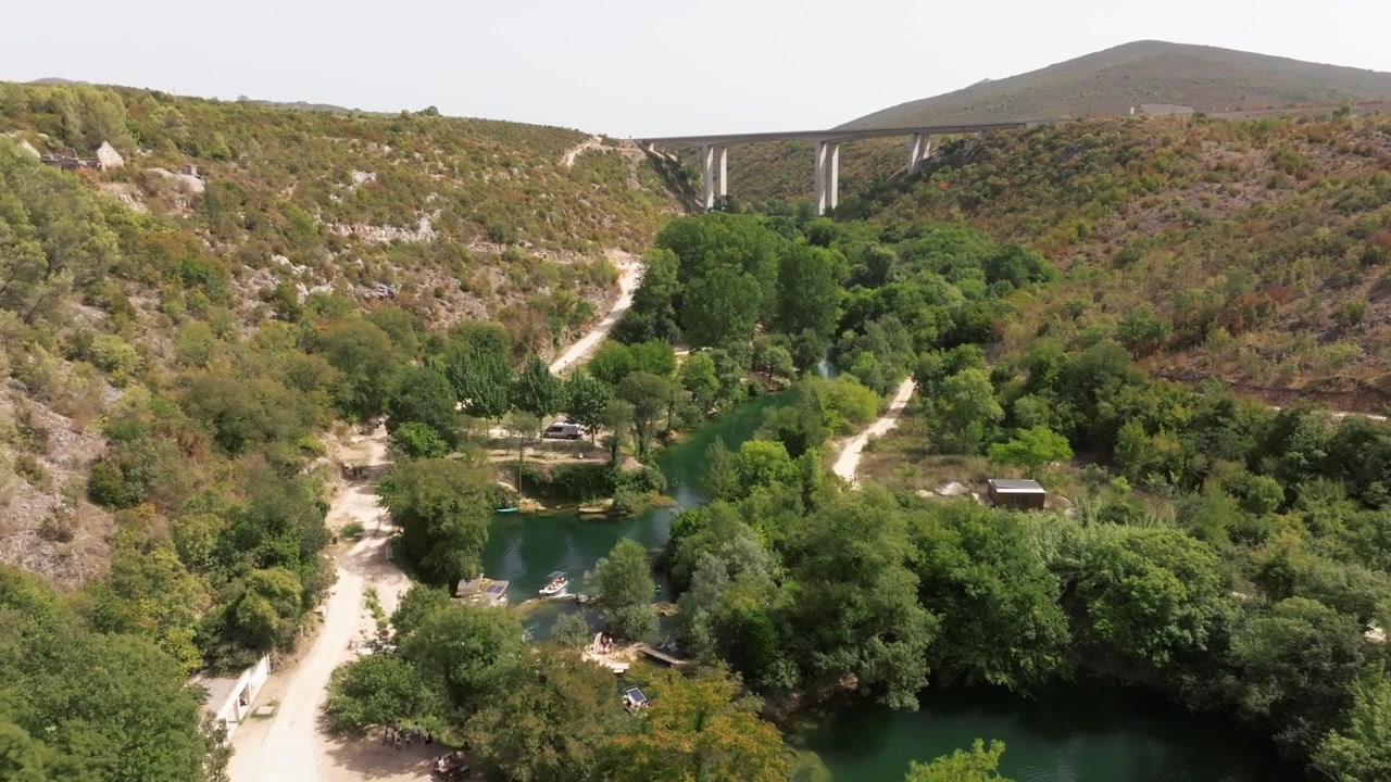 Piscine fluviali verdi, rive boscose e un alto viadotto in cemento attraversano un canyon asciutto mentre il drone scivola in avanti sopra quest'area balneare rurale